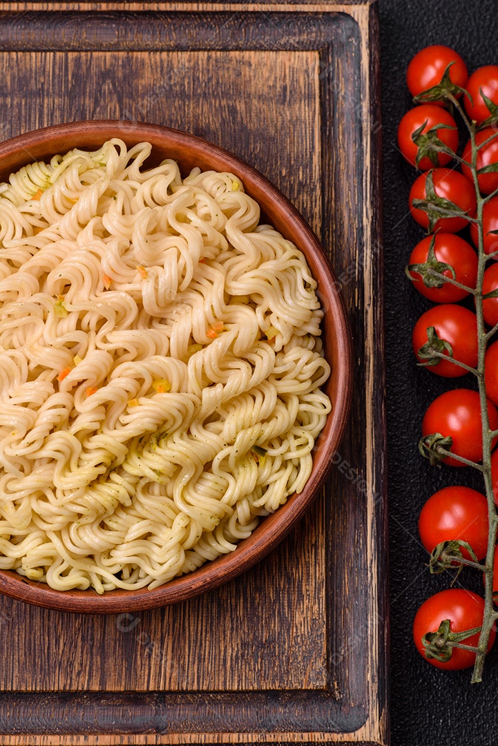 Delicioso macarrão de arroz asiático ou udon com legumes, especiarias e ervas sobre um fundo escuro de concreto