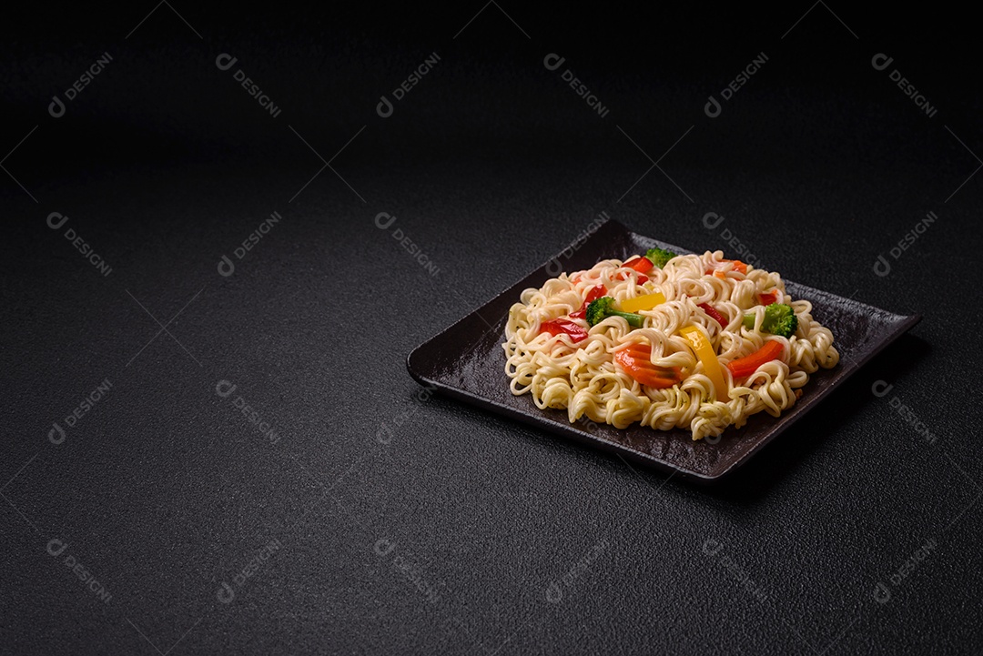 Delicioso macarrão de arroz asiático ou udon com legumes, especiarias e ervas sobre um fundo escuro de concreto