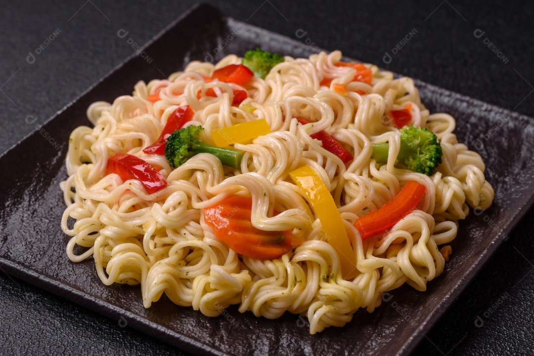Delicioso macarrão de arroz asiático ou udon com legumes, especiarias e ervas sobre um fundo escuro de concreto