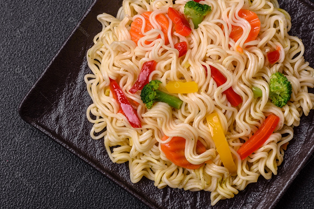 Delicioso macarrão de arroz asiático ou udon com legumes, especiarias e ervas sobre um fundo escuro de concreto