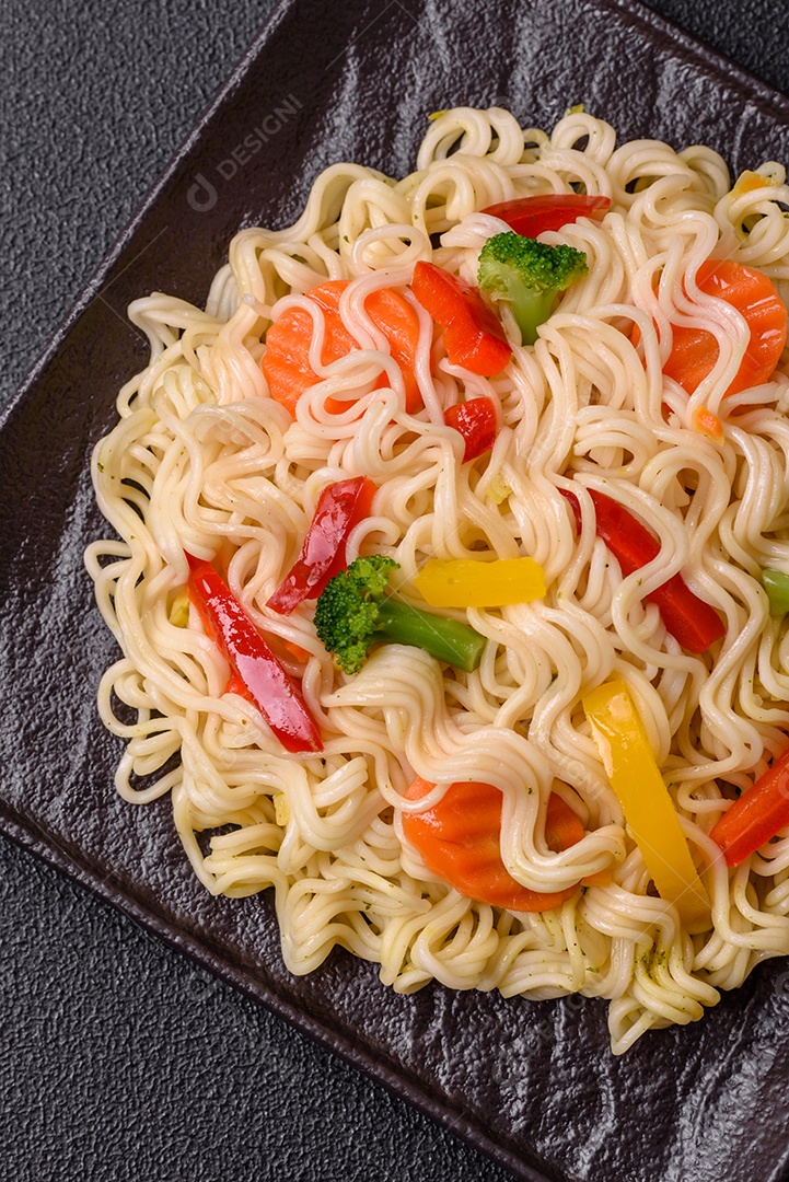 Delicioso macarrão de arroz asiático ou udon com legumes, especiarias e ervas sobre um fundo escuro de concreto