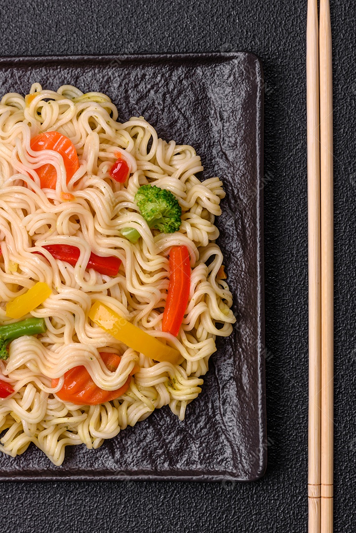 Delicioso macarrão de arroz asiático ou udon com legumes, especiarias e ervas sobre um fundo escuro de concreto