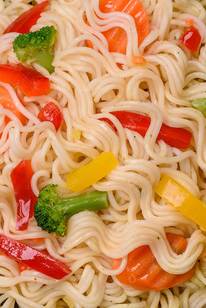 Delicioso macarrão de arroz asiático ou udon com legumes, especiarias e ervas sobre um fundo escuro de concreto