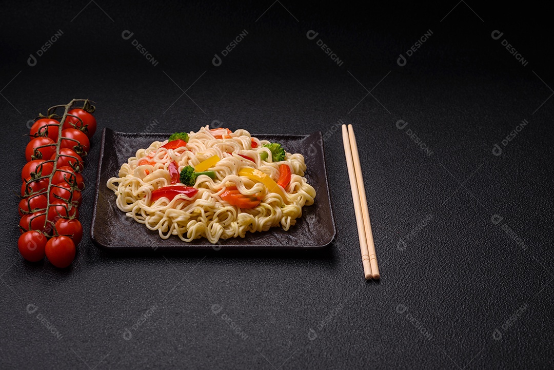 Delicioso macarrão de arroz asiático ou udon com legumes, especiarias e ervas sobre um fundo escuro de concreto