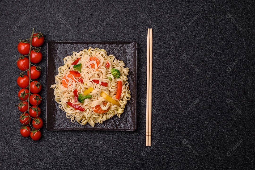 Delicioso macarrão de arroz asiático ou udon com legumes, especiarias e ervas sobre um fundo escuro de concreto