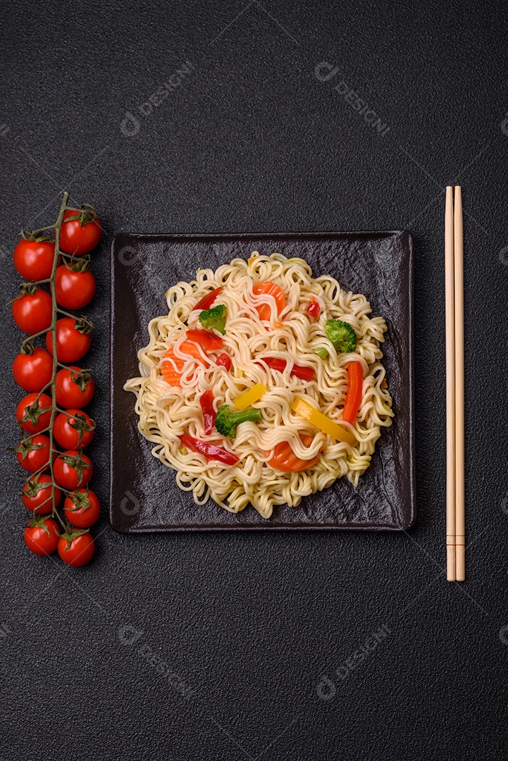 Delicioso macarrão de arroz asiático ou udon com legumes, especiarias e ervas sobre um fundo escuro de concreto