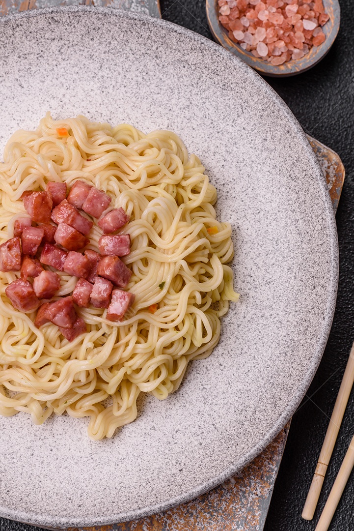 Delicioso macarrão de arroz asiático ou udon com legumes, especiarias e ervas sobre um fundo escuro de concreto