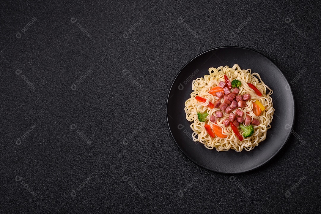 Delicioso macarrão de arroz asiático ou udon com legumes, especiarias e ervas sobre um fundo escuro de concreto