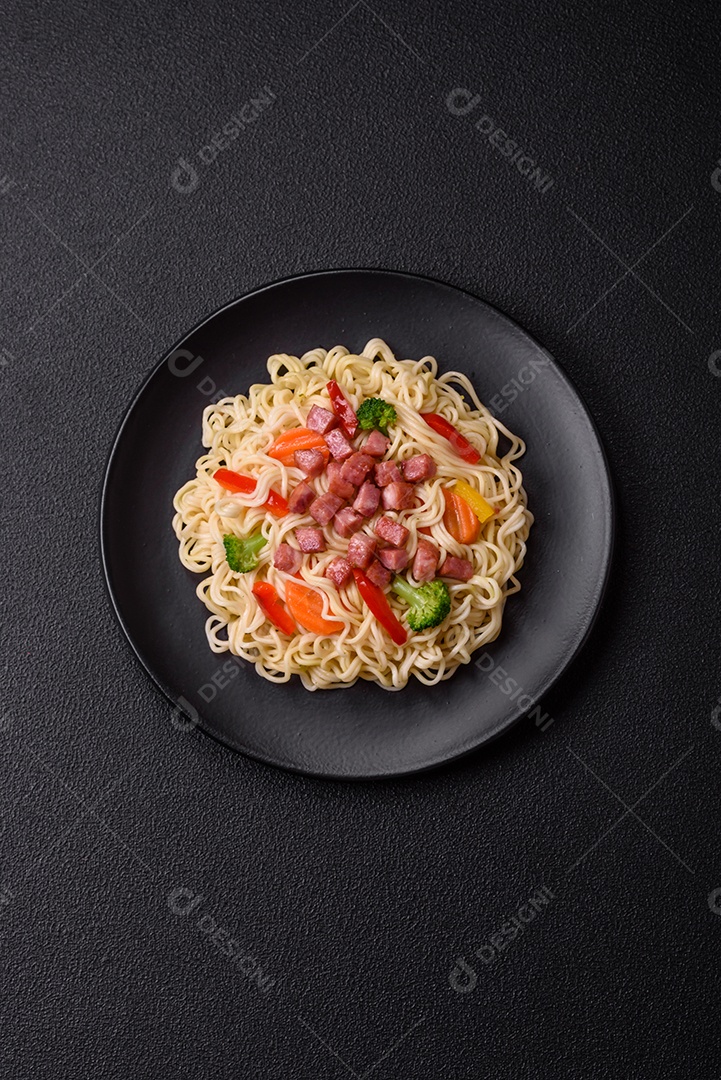 Delicioso macarrão de arroz asiático ou udon com legumes, especiarias e ervas sobre um fundo escuro de concreto