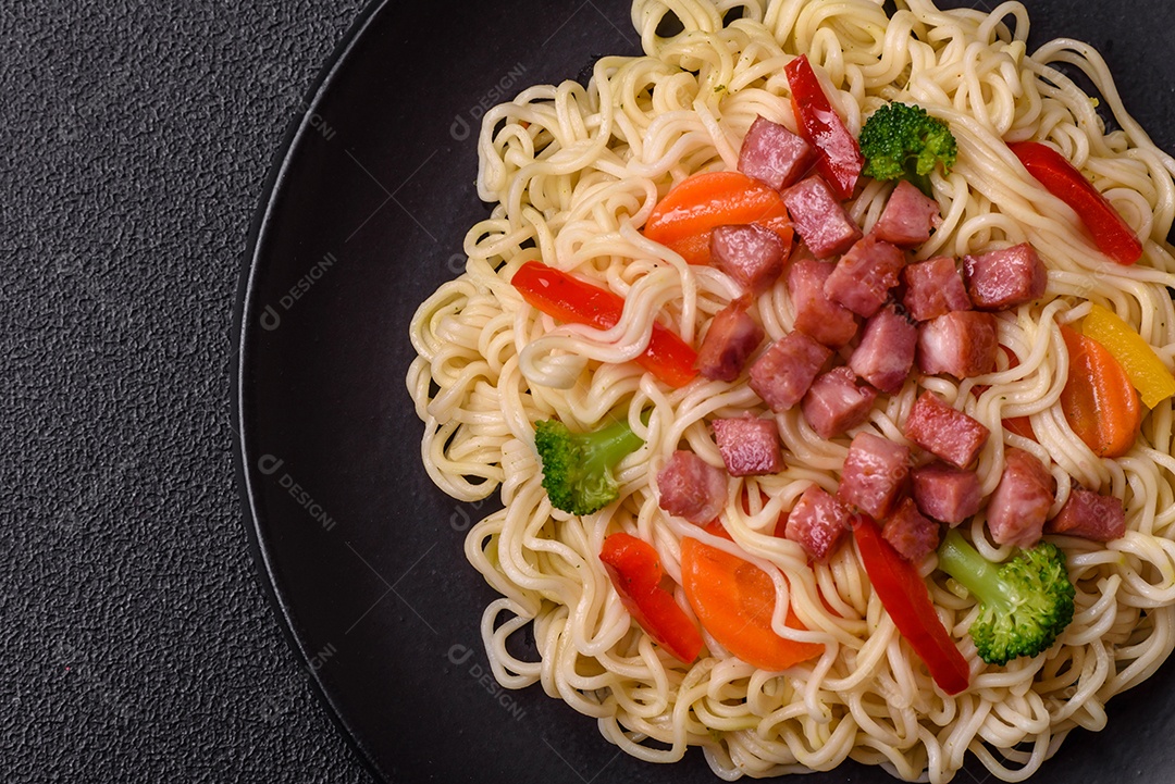 Delicioso macarrão de arroz asiático ou udon com legumes, especiarias e ervas sobre um fundo escuro de concreto