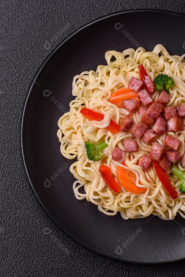 Delicioso macarrão de arroz asiático ou udon com legumes, especiarias e ervas sobre um fundo escuro de concreto