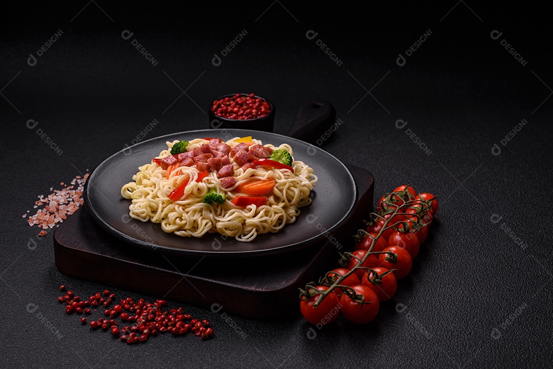 Delicioso macarrão de arroz asiático ou udon com legumes, especiarias e ervas sobre um fundo escuro de concreto