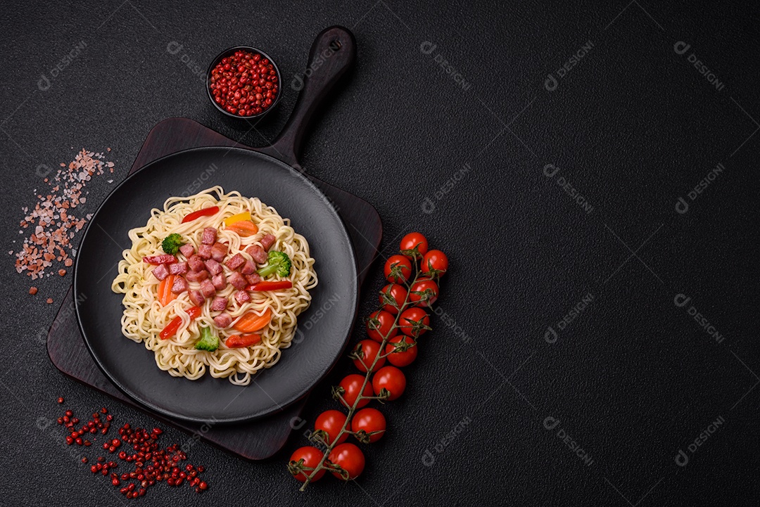 Delicioso macarrão de arroz asiático ou udon com legumes, especiarias e ervas sobre um fundo escuro de concreto
