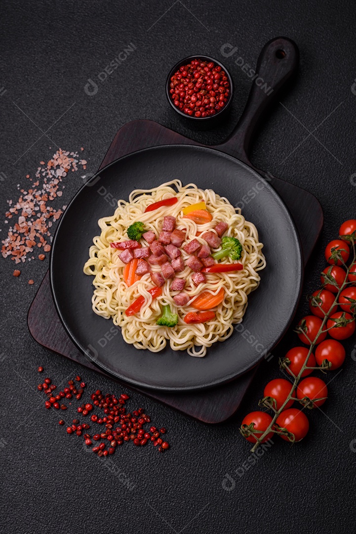 Delicioso macarrão de arroz asiático ou udon com legumes, especiarias e ervas sobre um fundo escuro de concret