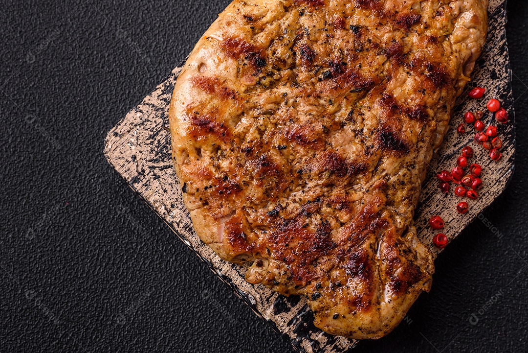 Delicioso bife de porco suculento com sal, especiarias e ervas sobre um fundo escuro de concreto