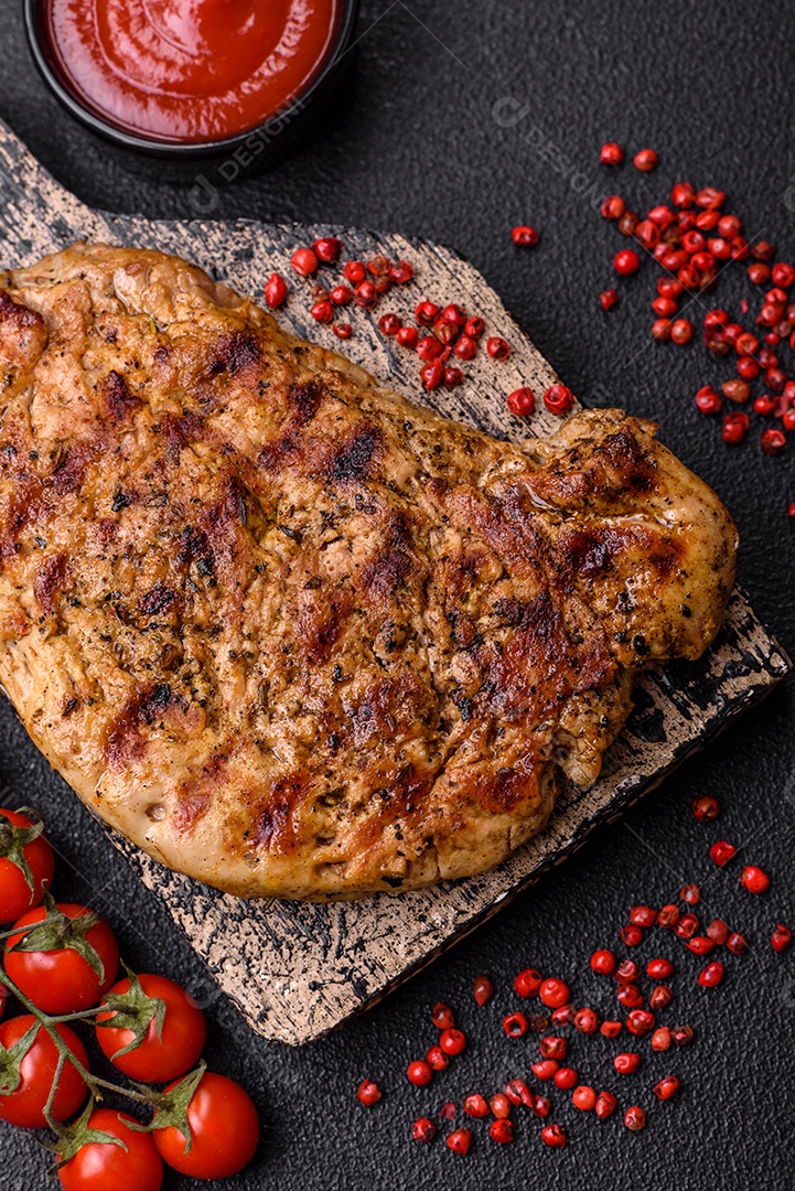 Delicioso bife de porco suculento com sal, especiarias e ervas sobre um fundo escuro de concreto