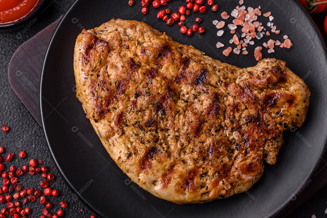 Delicioso bife de porco suculento com sal, especiarias e ervas sobre um fundo escuro de concreto