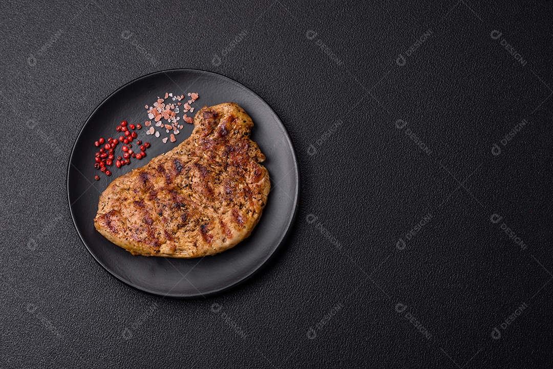 Delicioso bife de porco suculento com sal, especiarias e ervas sobre um fundo escuro de concreto