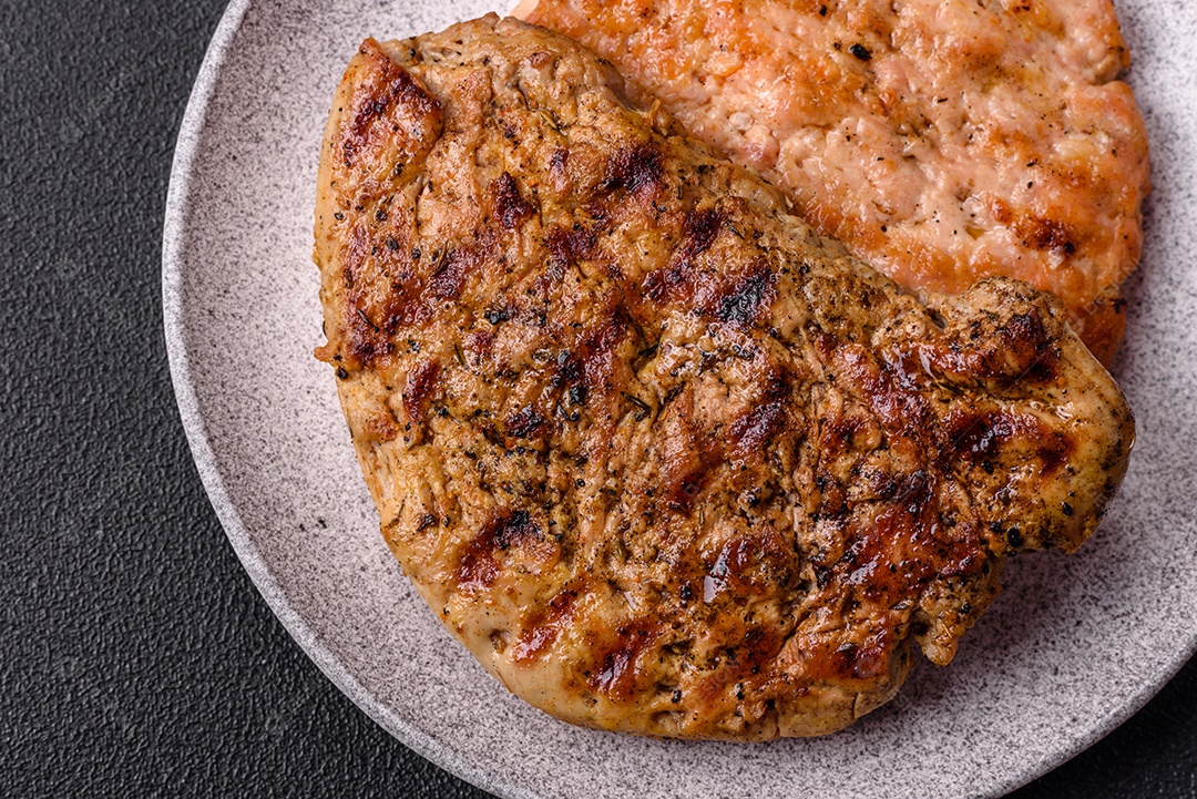 Delicioso bife de porco suculento com sal, especiarias e ervas sobre um fundo escuro de concreto