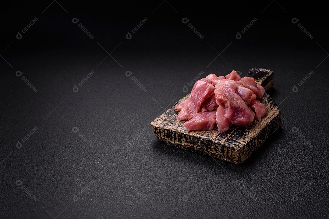 Fatias de carne crua de porco ou peru com sal, especiarias e ervas sobre um fundo escuro de concreto