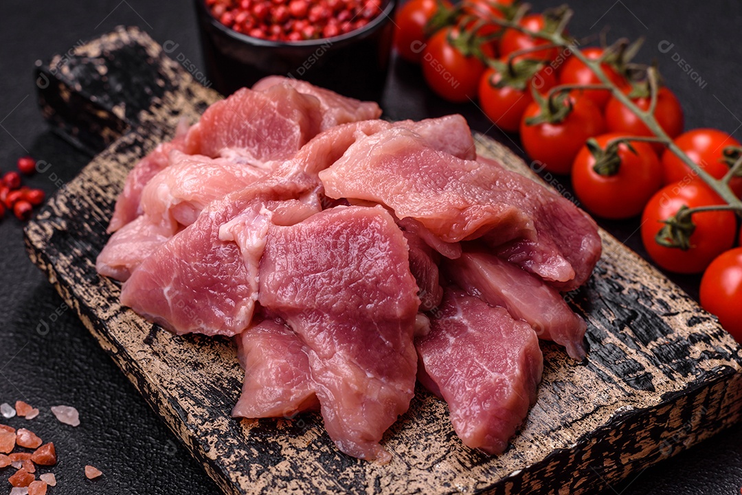 Fatias de carne crua de porco ou peru com sal, especiarias e ervas sobre um fundo escuro de concreto