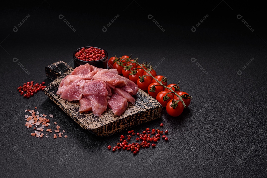 Fatias de carne crua de porco ou peru com sal, especiarias e ervas sobre um fundo escuro de concreto