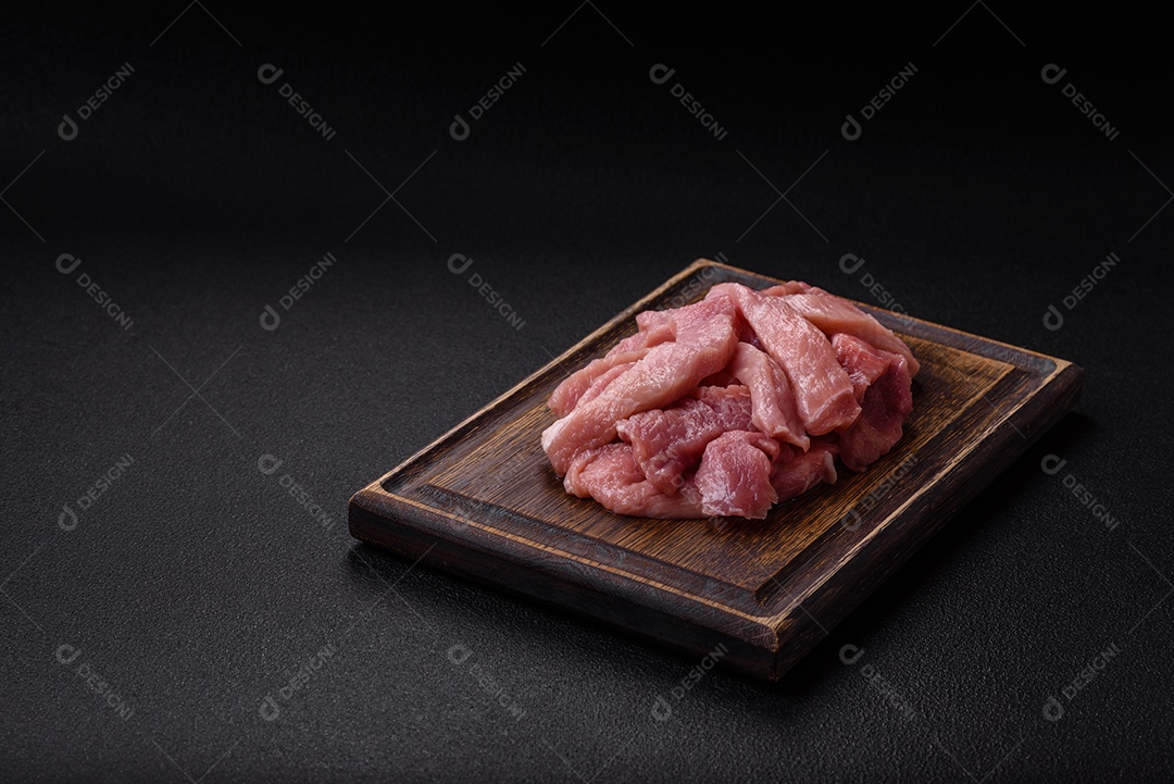 Fatias de carne crua de porco ou peru com sal, especiarias e ervas sobre um fundo escuro de concreto