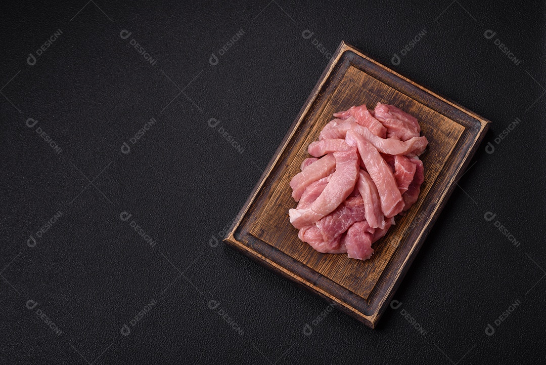 Fatias de carne crua de porco ou peru com sal, especiarias e ervas sobre um fundo escuro de concreto