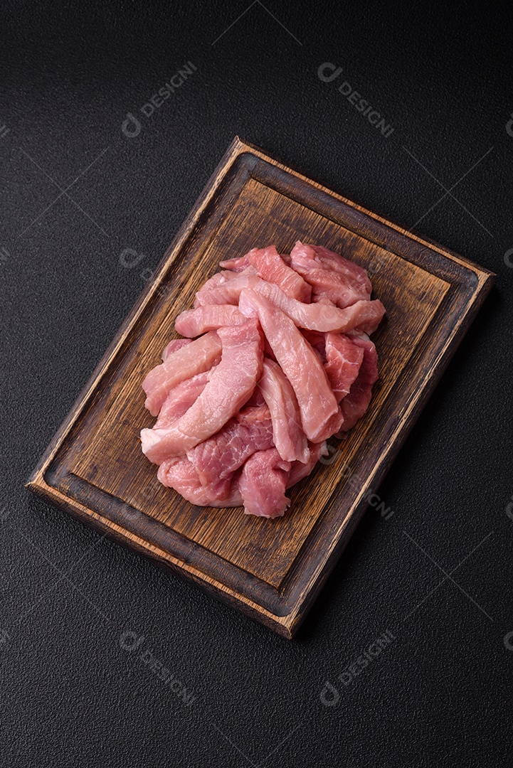 Fatias de carne crua de porco ou peru com sal, especiarias e ervas sobre um fundo escuro de concreto