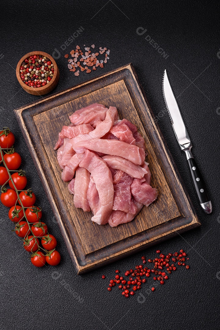 Fatias de carne crua de porco ou peru com sal, especiarias e ervas sobre um fundo escuro de concreto