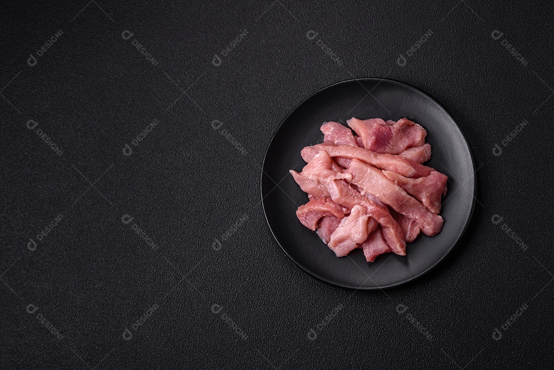 Fatias de carne crua de porco ou peru com sal, especiarias e ervas sobre um fundo escuro de concreto