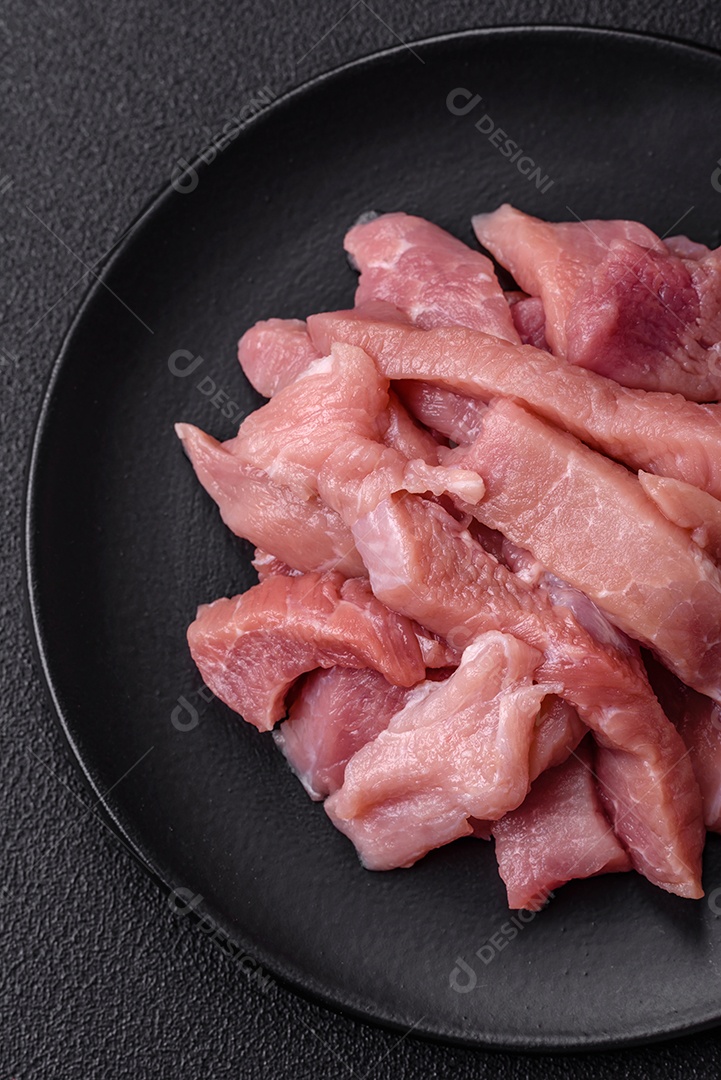 Fatias de carne crua de porco ou peru com sal, especiarias e ervas sobre um fundo escuro de concreto