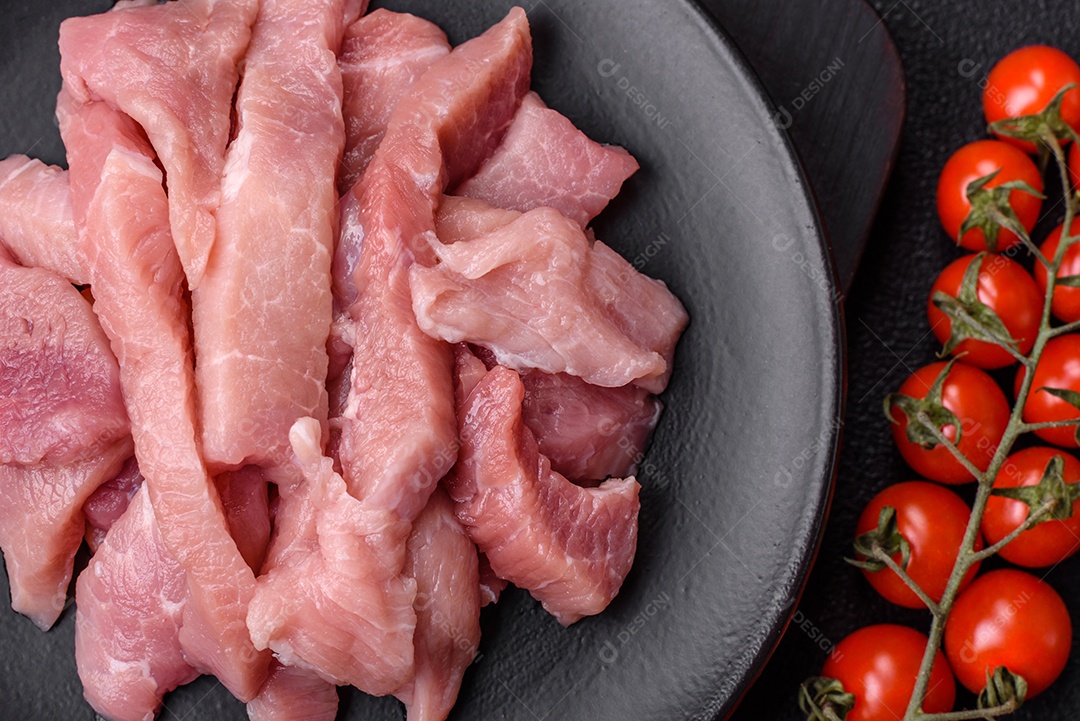 Fatias de carne crua de porco ou peru com sal, especiarias e ervas sobre um fundo escuro de concreto