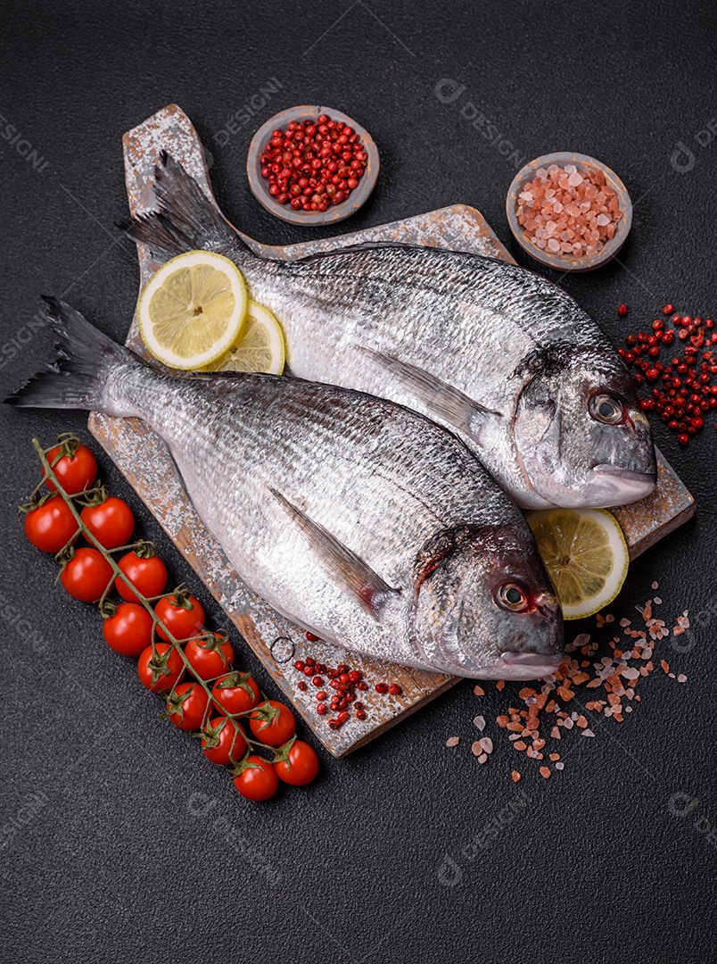 Peixe dourado cru inteiro com limão, sal, especiarias e ervas sobre um fundo escuro de concreto