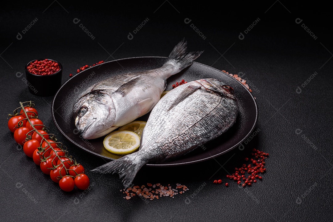 Peixe dourado cru inteiro com limão, sal, especiarias e ervas sobre um fundo escuro de concreto