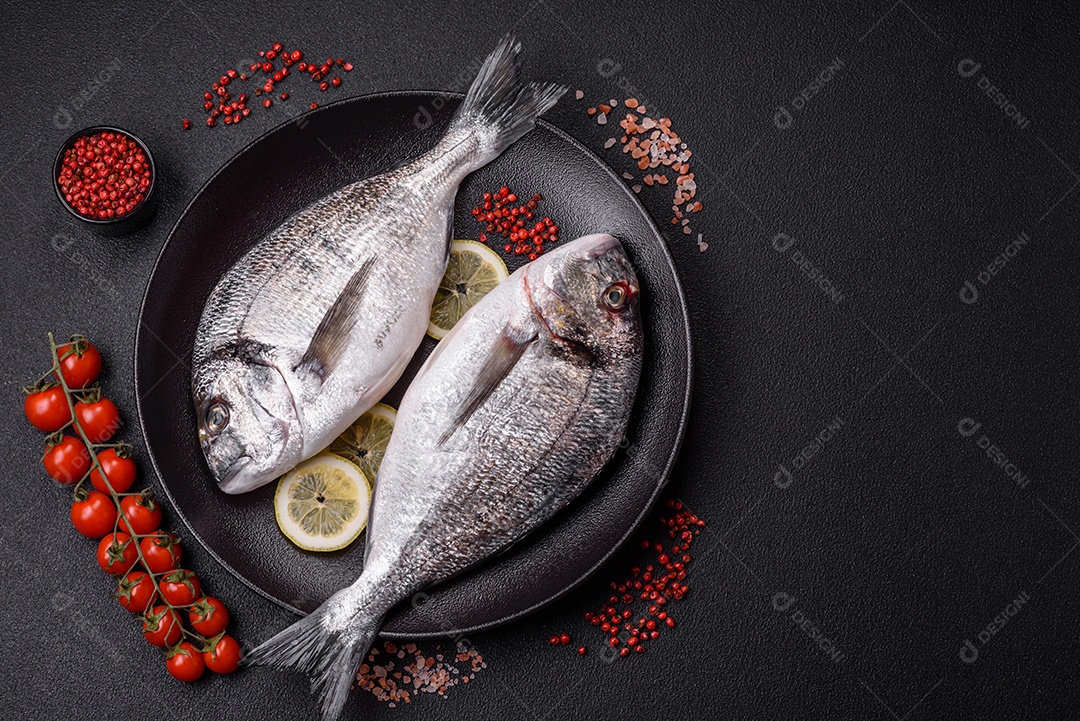 Peixe dourado cru inteiro com limão, sal, especiarias e ervas sobre um fundo escuro de concreto