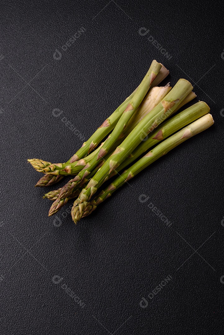Raminhos de espargos verdes crus como ingrediente para preparar um café da manhã saudável sobre um fundo escuro de concreto