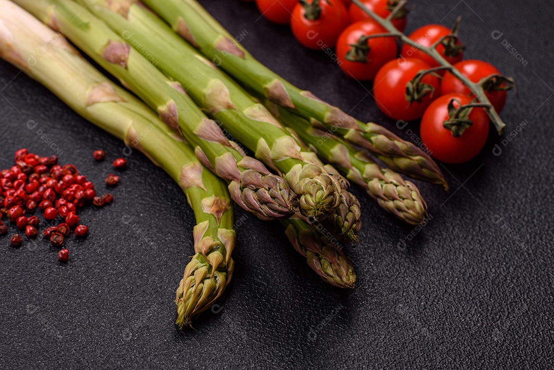 Raminhos de espargos verdes crus como ingrediente para preparar um café da manhã saudável sobre um fundo escuro de concreto