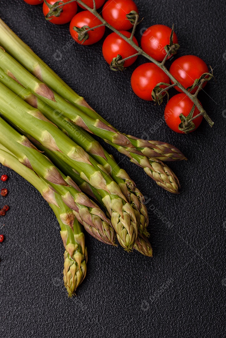 Raminhos de espargos verdes crus como ingrediente para preparar um café da manhã saudável sobre um fundo escuro de concreto