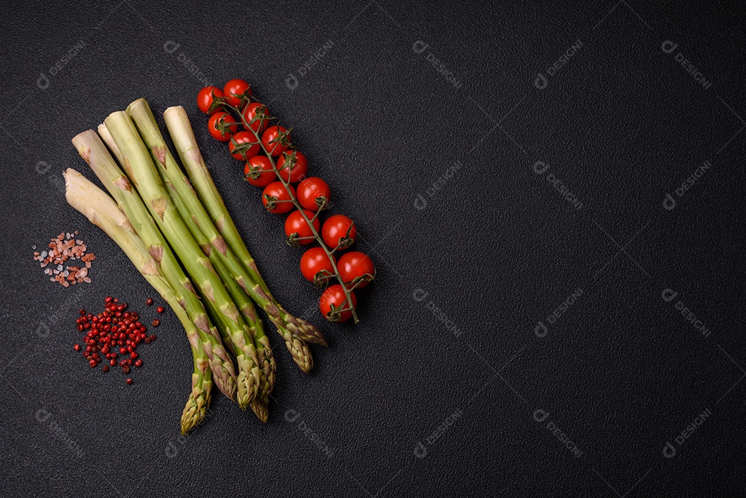 Raminhos de espargos verdes crus como ingrediente para preparar um café da manhã saudável sobre um fundo escuro de concreto