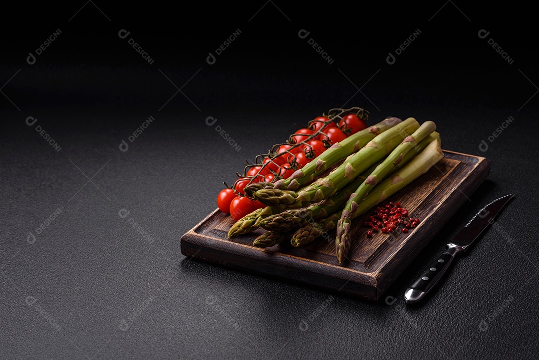 Raminhos de espargos verdes crus como ingrediente para preparar um café da manhã saudável sobre um fundo escuro de concreto