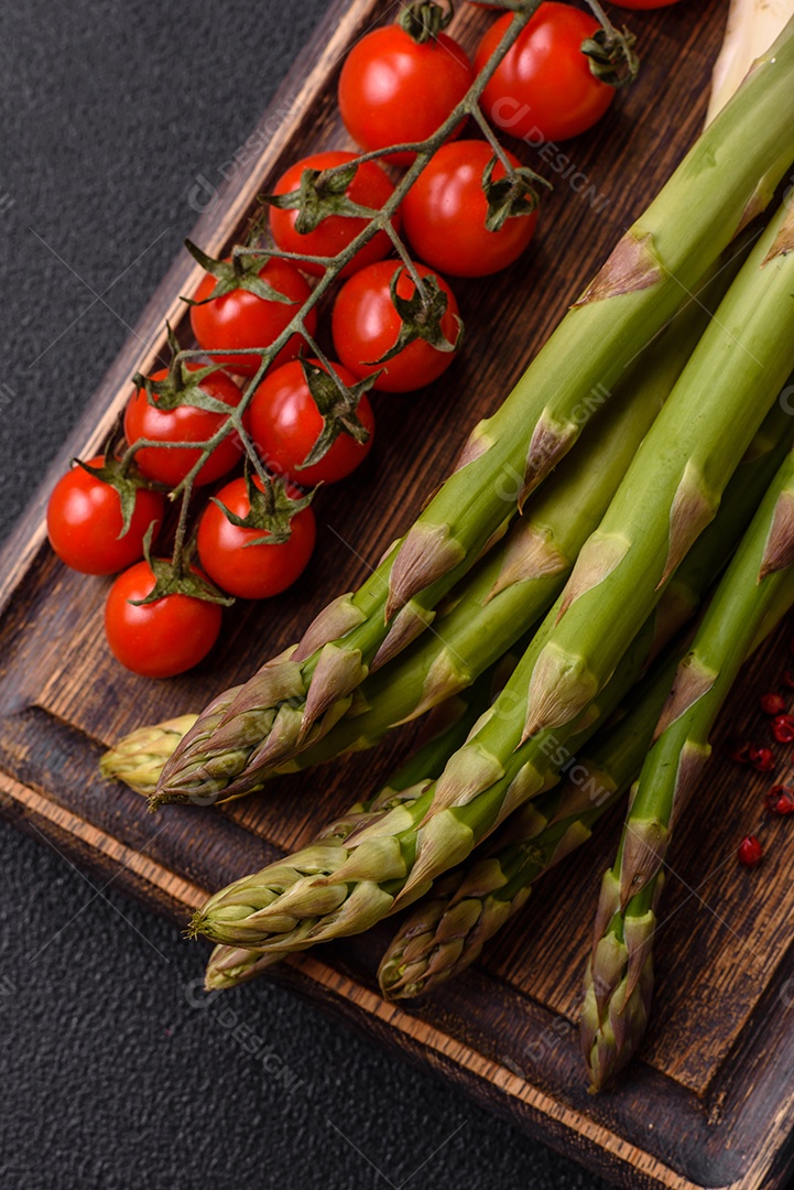 Raminhos de espargos verdes crus como ingrediente para preparar um café da manhã saudável sobre um fundo escuro de concreto