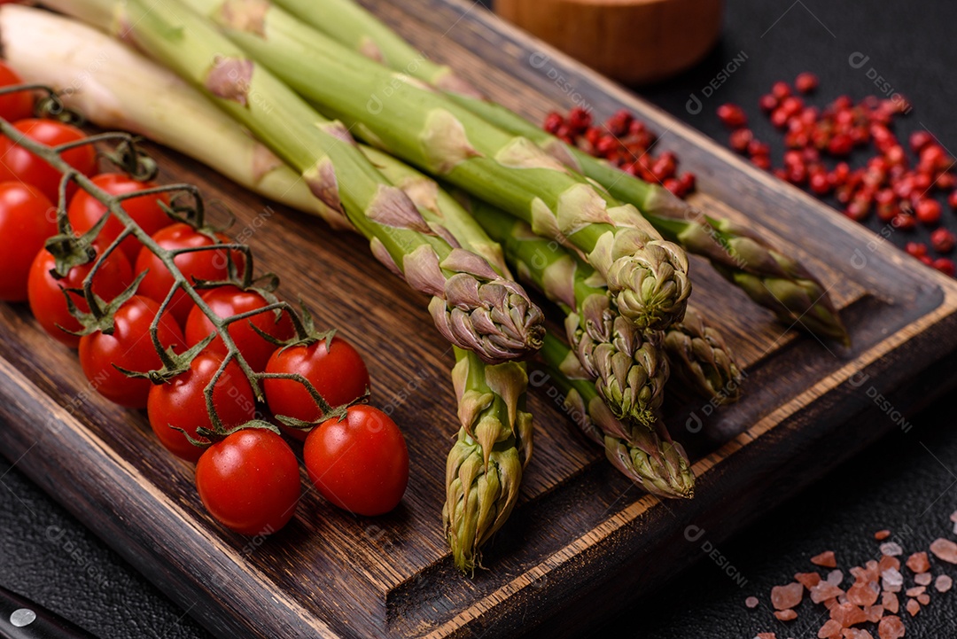 Raminhos de espargos verdes crus como ingrediente para preparar um café da manhã saudável sobre um fundo escuro de concreto