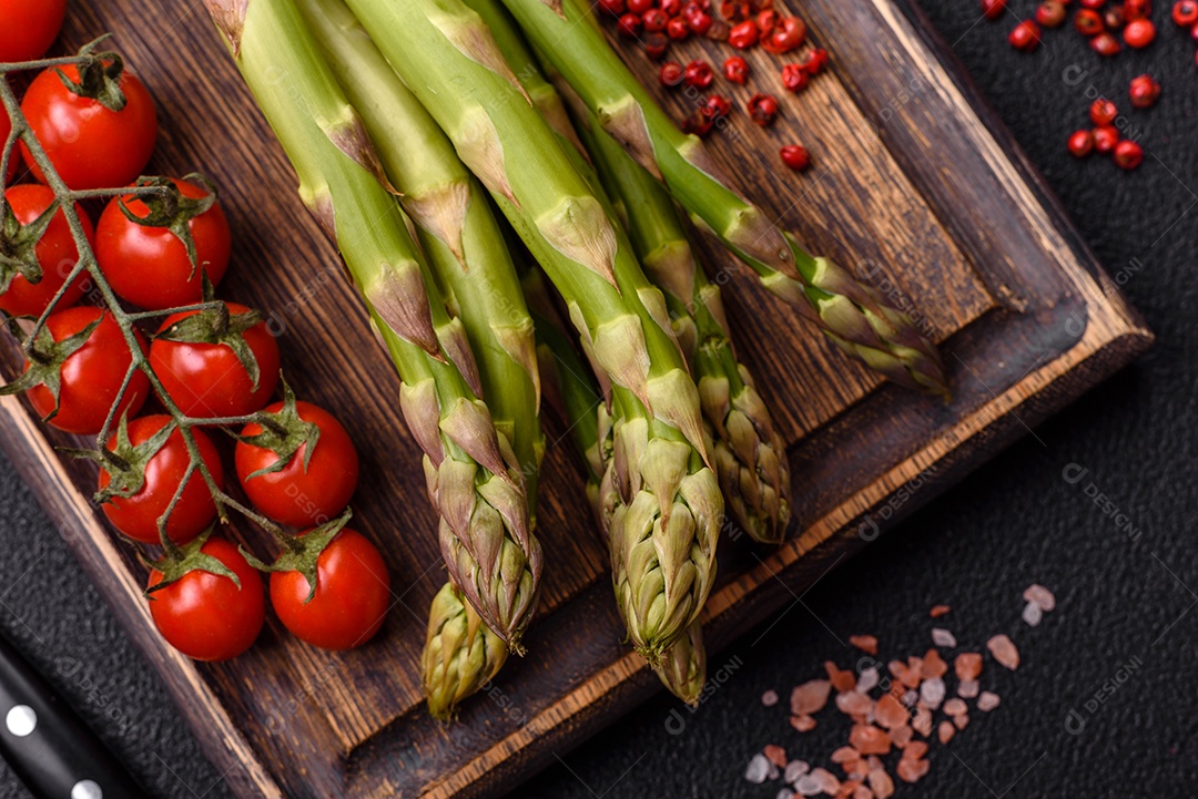 Raminhos de espargos verdes crus como ingrediente para preparar um café da manhã saudável sobre um fundo escuro de concreto