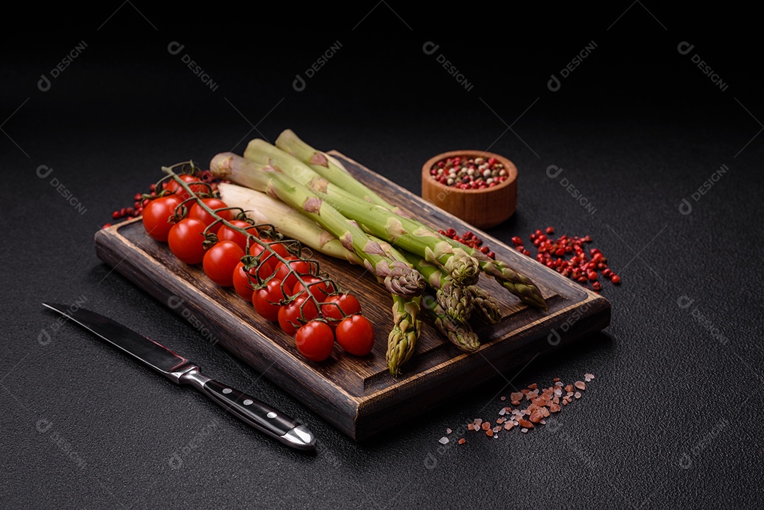 Raminhos de espargos verdes crus como ingrediente para preparar um café da manhã saudável sobre um fundo escuro de concreto