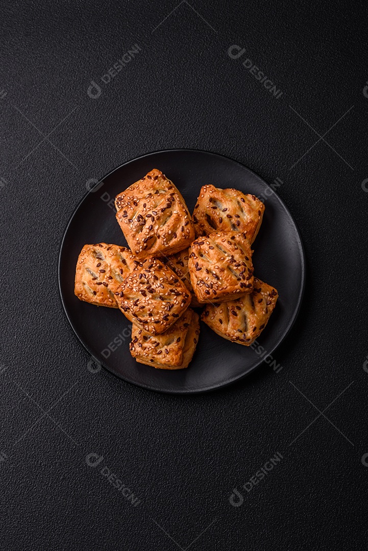 Folhados triangulares com queijo feta, tomate com sal, especiarias e ervas sobre fundo escuro de concreto