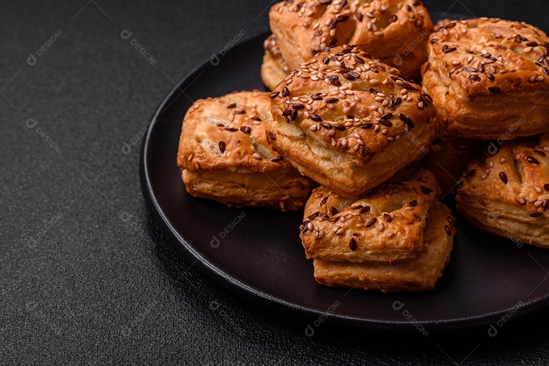 Folhados triangulares com queijo feta, tomate com sal, especiarias e ervas sobre fundo escuro de concreto