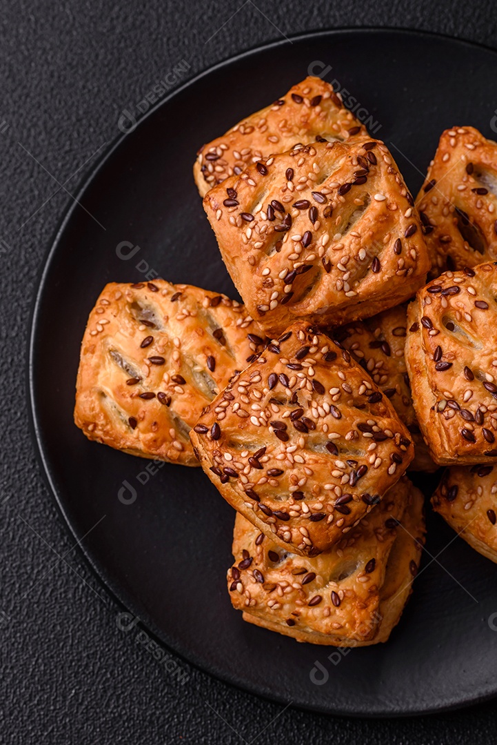 Folhados triangulares com queijo feta, tomate com sal, especiarias e ervas sobre fundo escuro de concreto