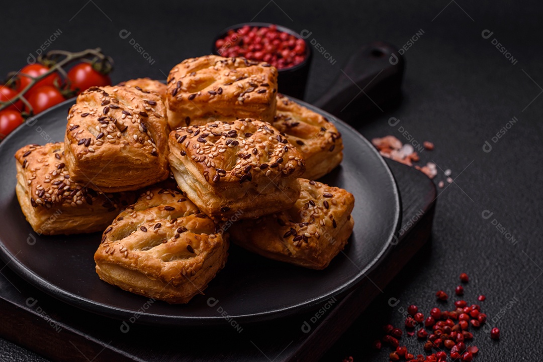 Folhados triangulares com queijo feta, tomate com sal, especiarias e ervas sobre fundo escuro de concreto