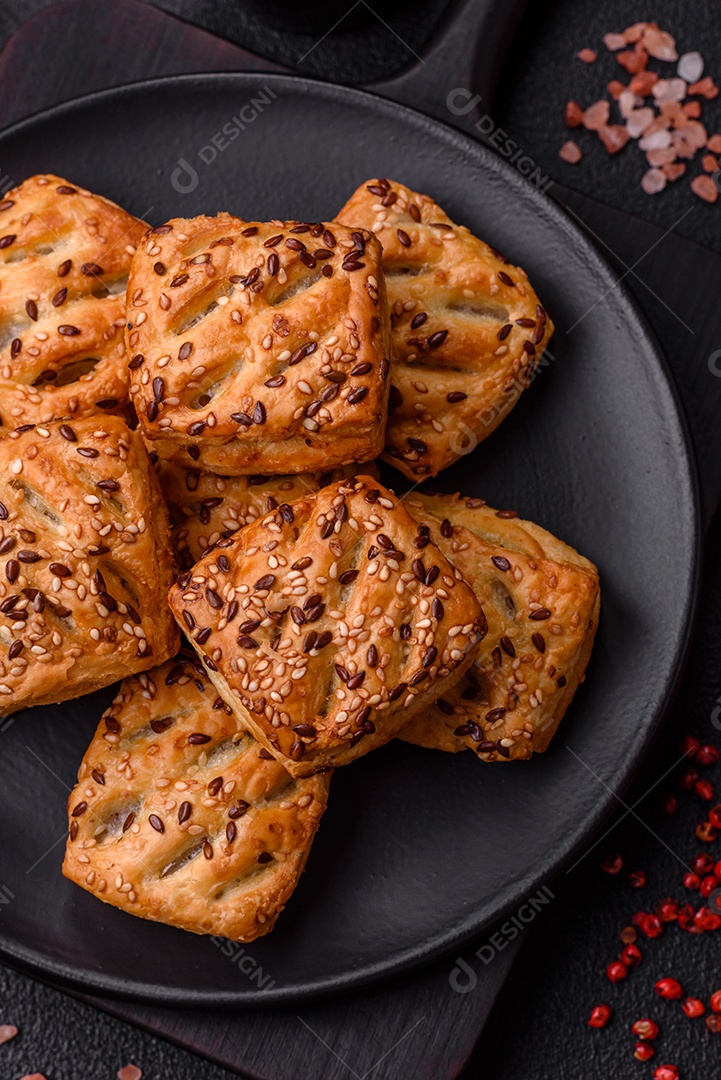 Folhados triangulares com queijo feta, tomate com sal, especiarias e ervas sobre fundo escuro de concreto